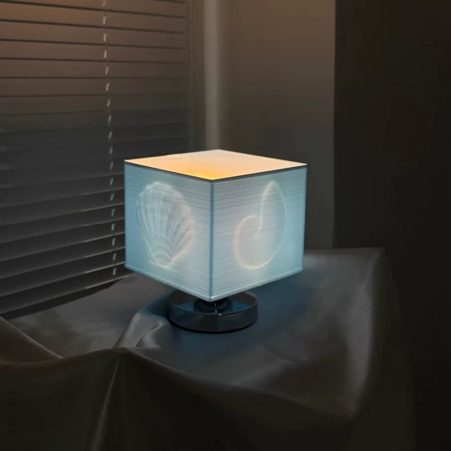 Cube-shaped lamp with a textured white shade on a dark surface.