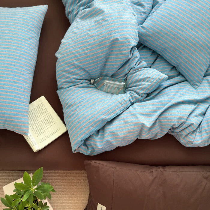 Blue striped bedding on a brown bed with a plant and book in the foreground