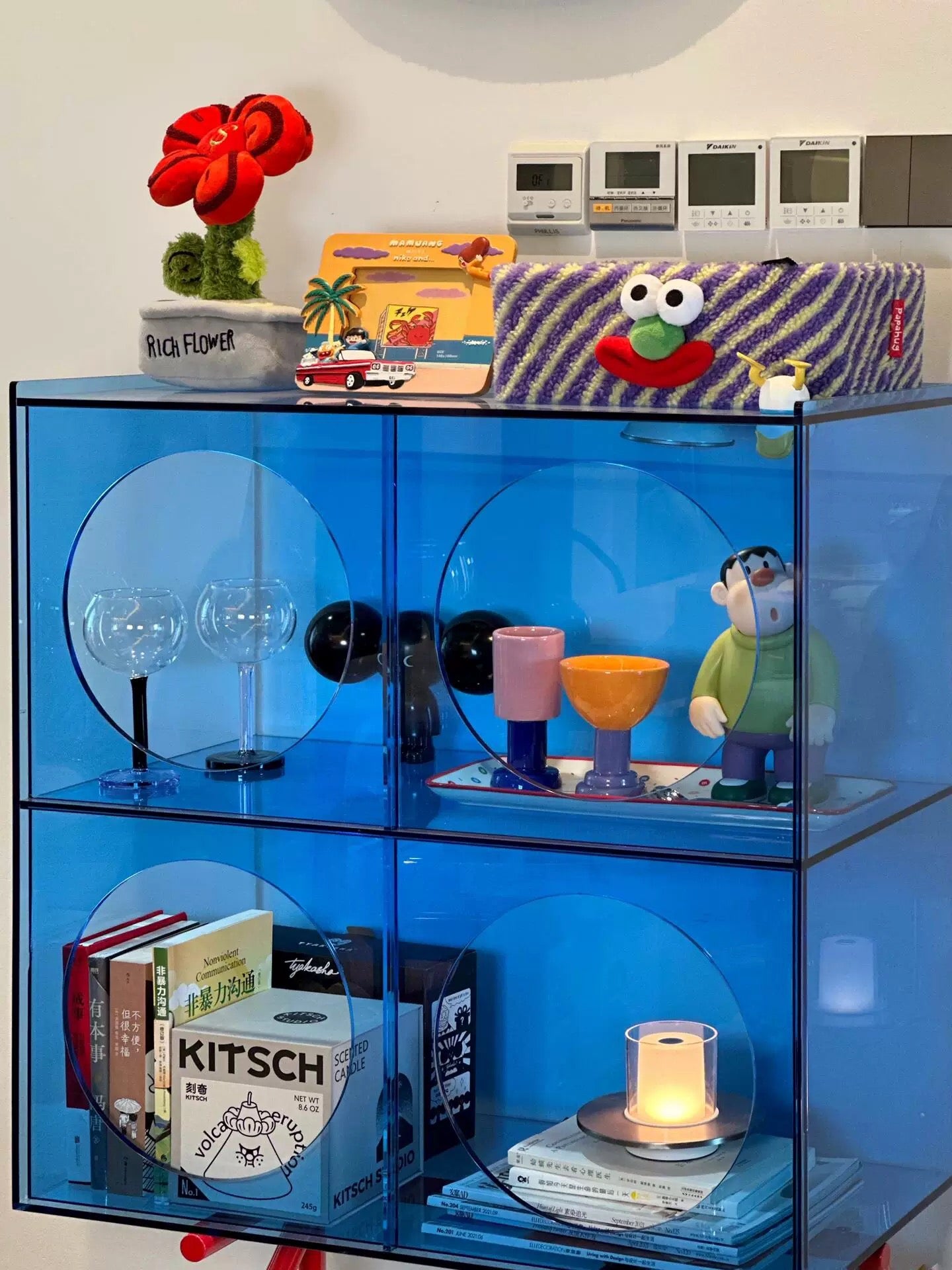 Blue transparent cube shelf with various decorative items including books, a candle, and small figurines.