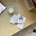 Phone cases with bow design on a wooden surface next to a phone and glass of water.