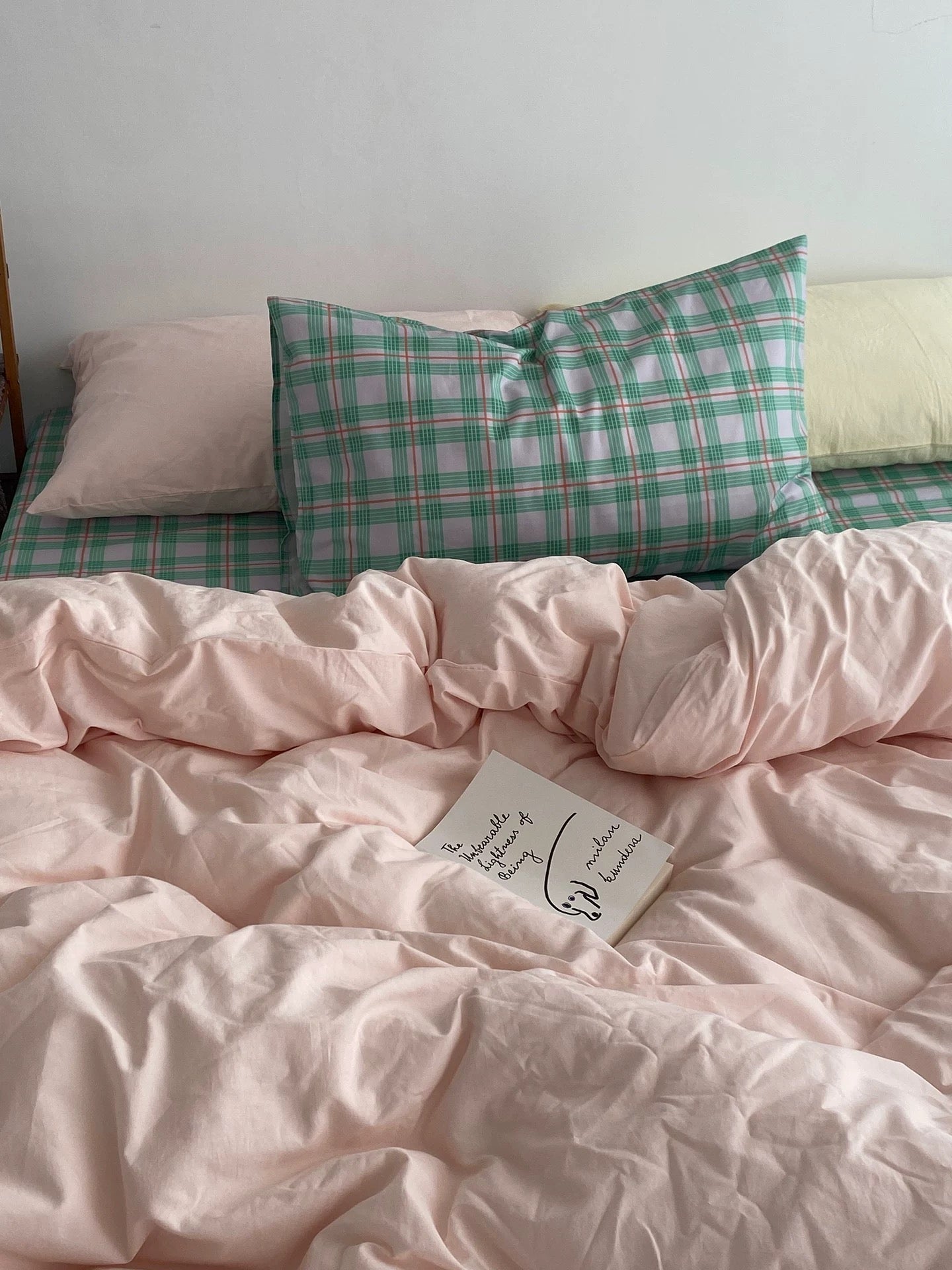 Bed with pink comforter and plaid pillows against a white wall