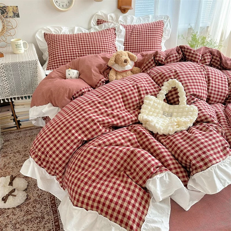 Red and white checkered bedding set on a bed with a teddy bear and decorative items.
