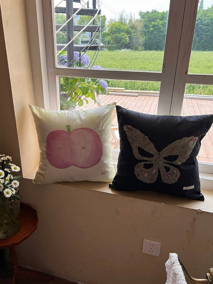 Accent pillows with pastel butterfly, gray butterfly and apple prints in a sunny corner