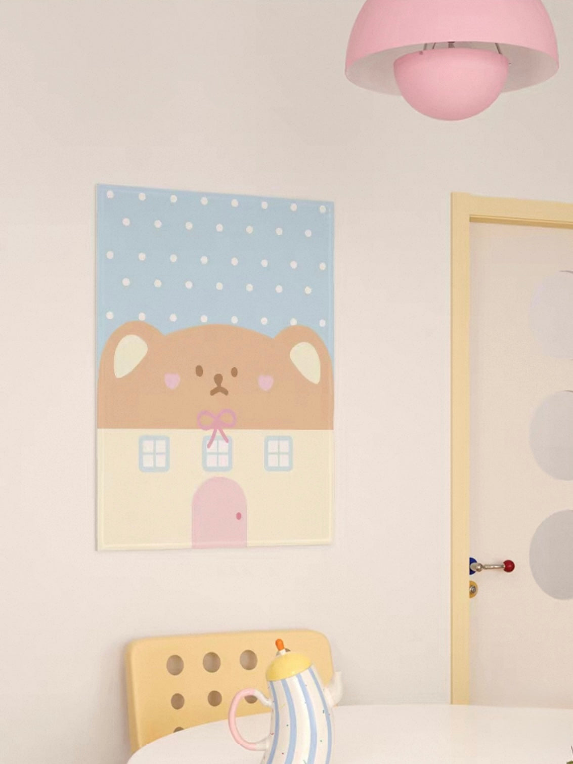 A bear house tapestry shows a bear face roof above a cream house with a pink door beneath a blue dotted panel.