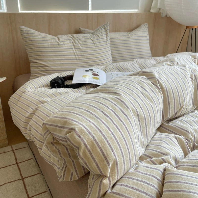 Beige and brown striped bedding on a bed with a window in the background.
