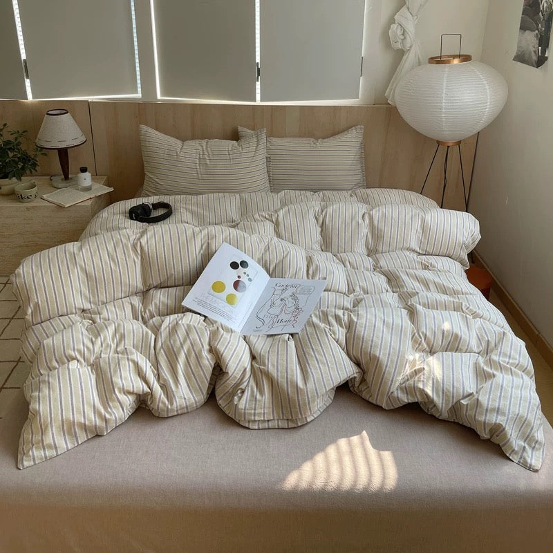 Bed with striped bedding and a book on a wooden floor with lamps and decor in the background.