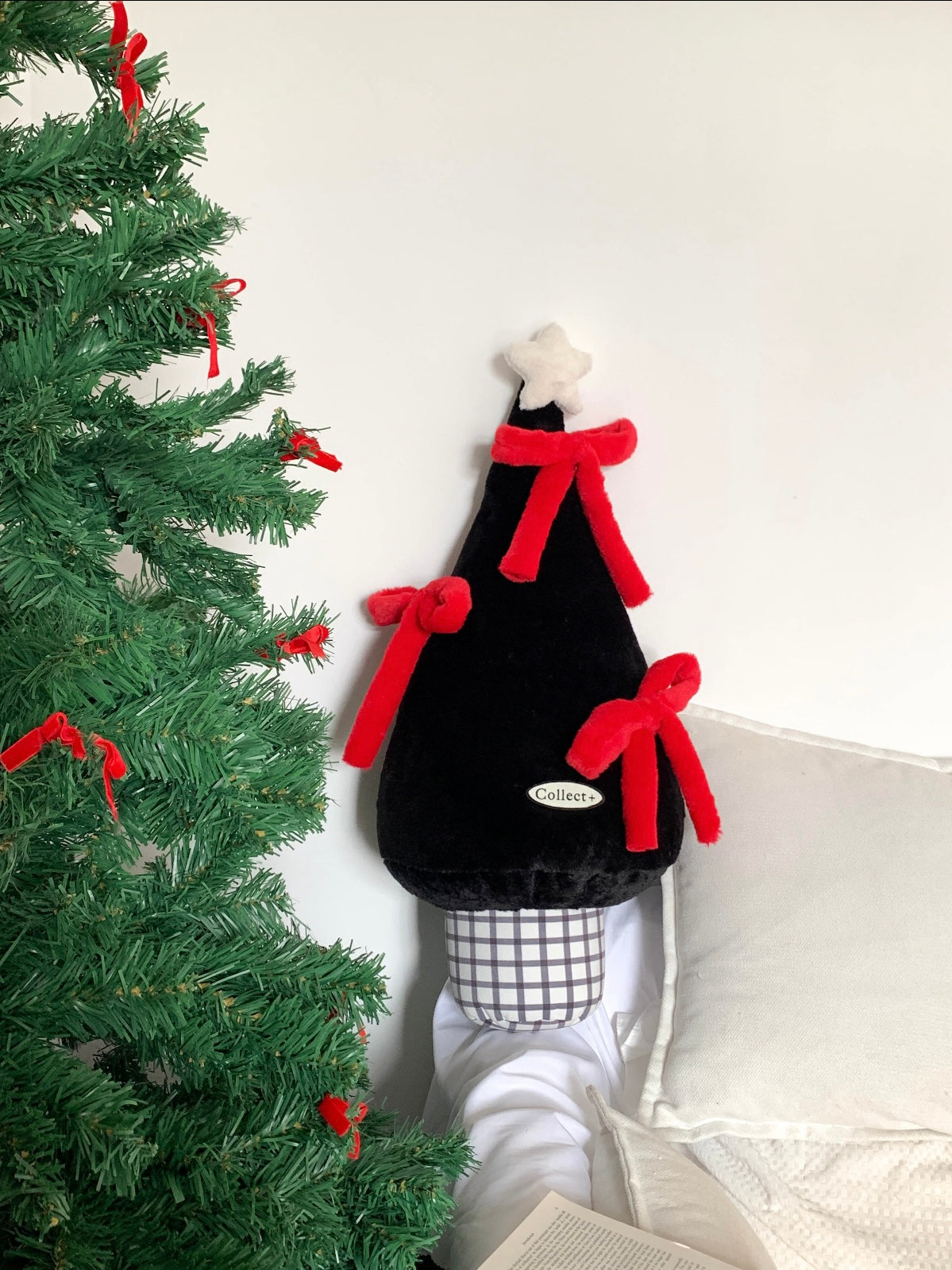 Black Christmas tree pillow with red bows styled beside a Christmas tree