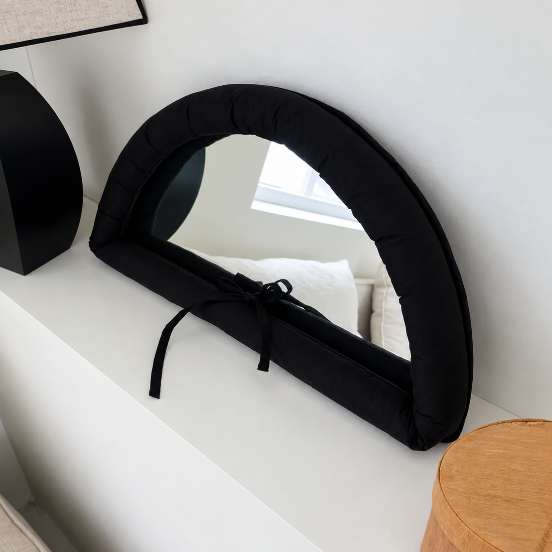 White bow mirror with a padded semicircular frame and matching ribbon, leaning against a dark background.