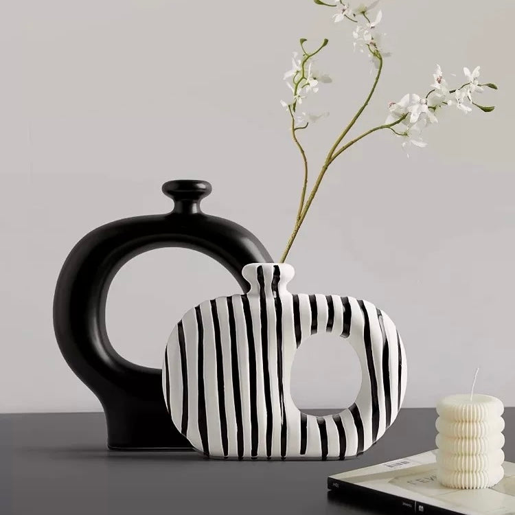 Two ceramic vases, one black and one with black and white striped pattern, on a light gray background.
