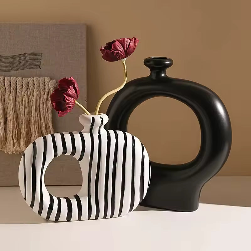 Black and white striped vase with a black round vase and red flowers on a beige surface.