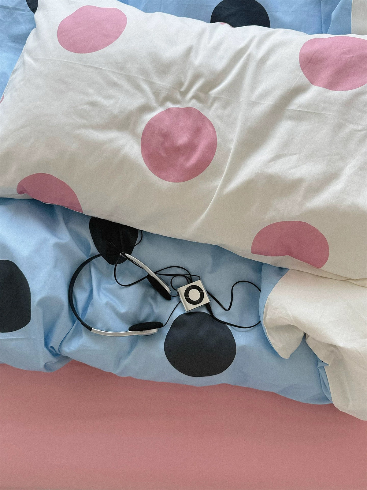 Folded blue and pink bedding shows large black dots beneath a cream pillowcase with pink dots.
