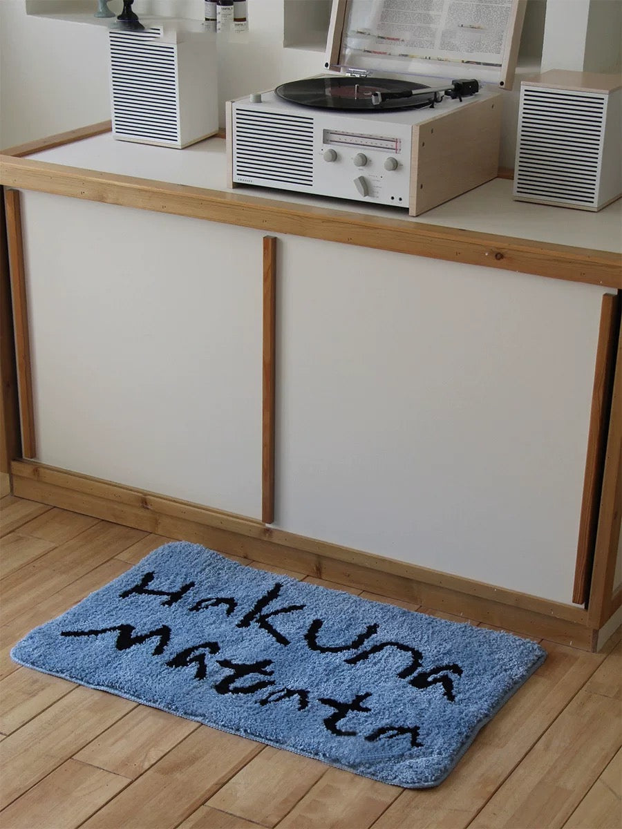 A funny bath mat in blue has black Hakuna Matata lettering and rounded corners on the kitchen floor.