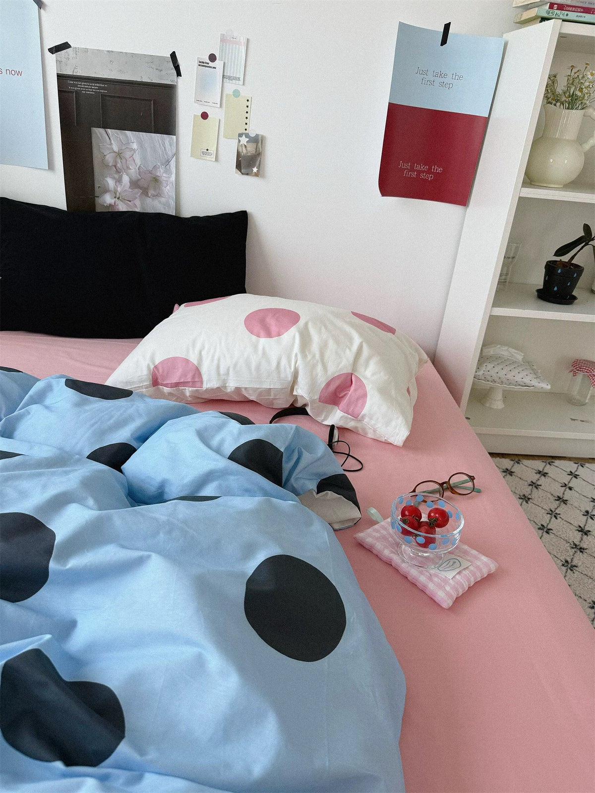 A black pillowcase and a cream pillowcase with large pink dots sit behind the blue dotted cover.