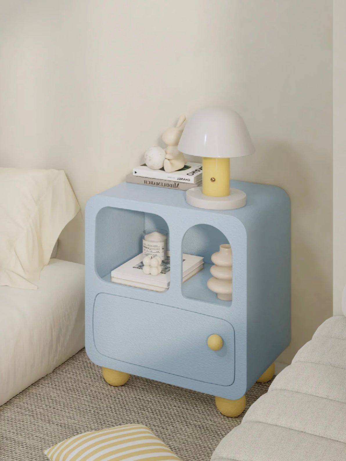 A blue bedside cabinet viewed at an angle shows its curved front openings, yellow knob and yellow feet.