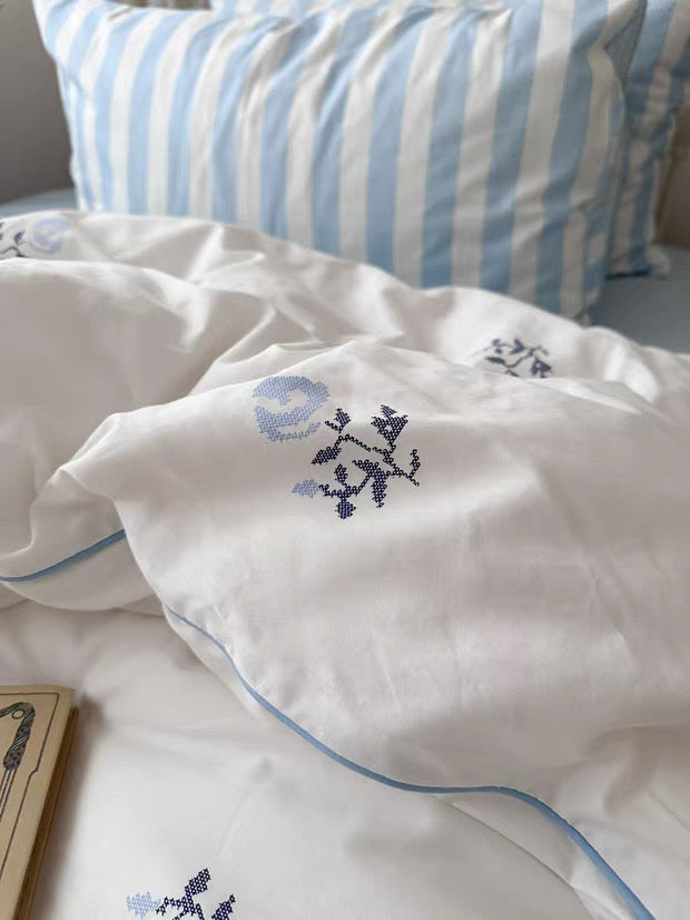 Embroidered pillowcases with floral designs on a bed with striped pillows.