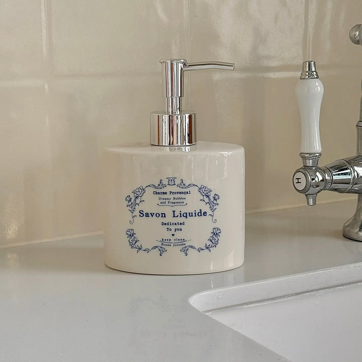A blue floral ceramic soap dispenser has decorative lettering inside a flower border beneath a silver pump.