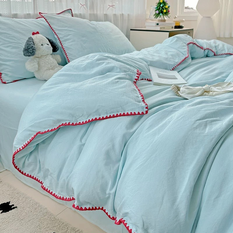 Light blue bedding set with red trim on a bed in a bright room.