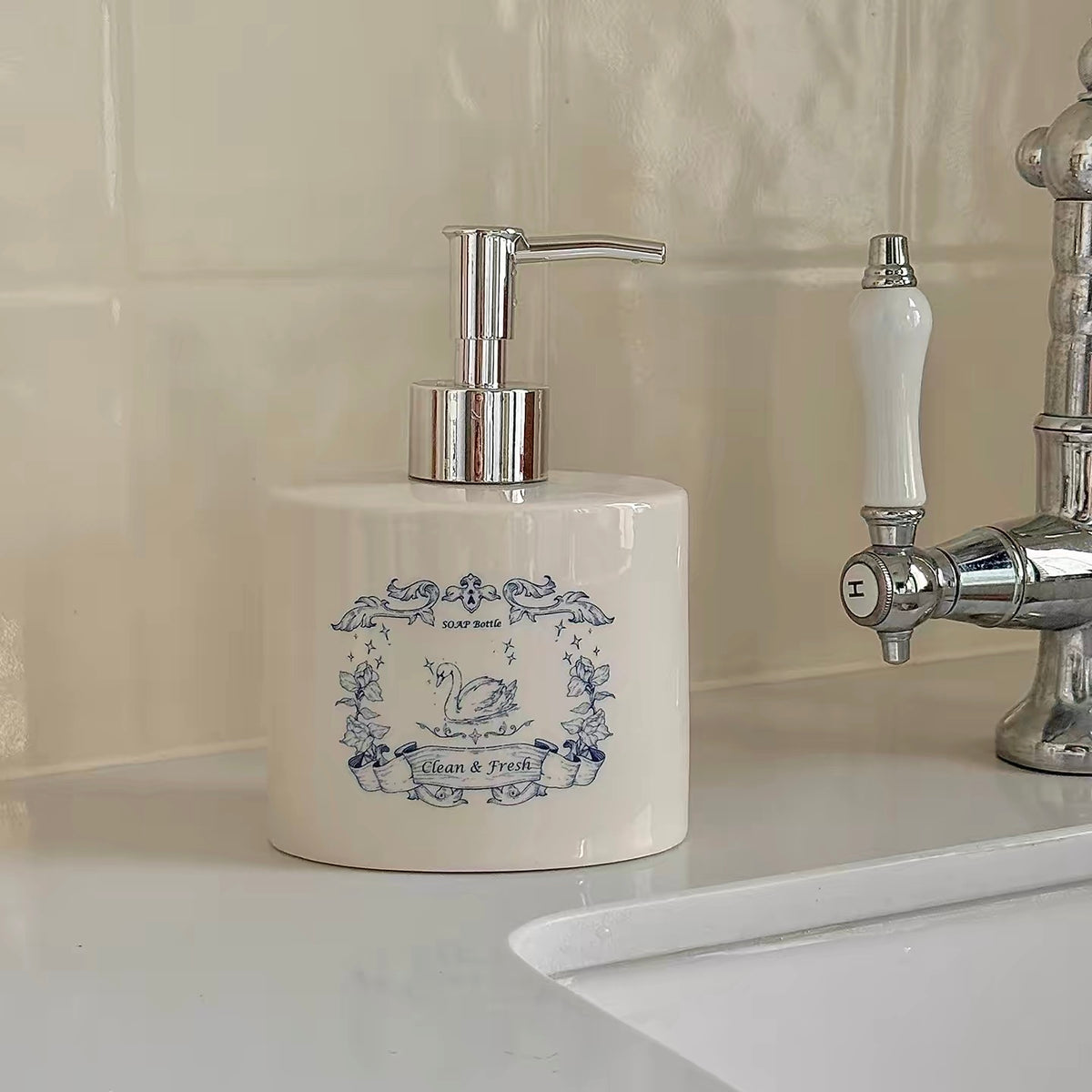 A blue swan soap dispenser shows a bird between flowers beneath a ribbon banner and silver pump.