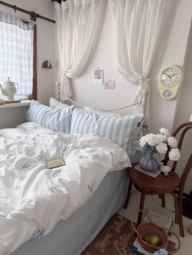 Bedroom with white canopy bed, striped pillows, and a clock on the wall.