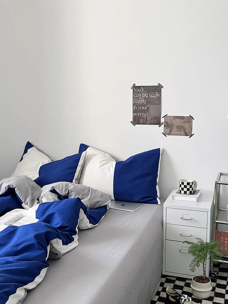 Bedroom with blue and gray bedding, nightstand, and decorative items on a white wall.