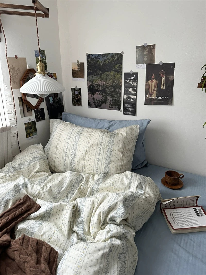 Breathable cotton bedding featuring delicate blue floral stripes styled inside bright European inspired bedroom with plants everywhere.