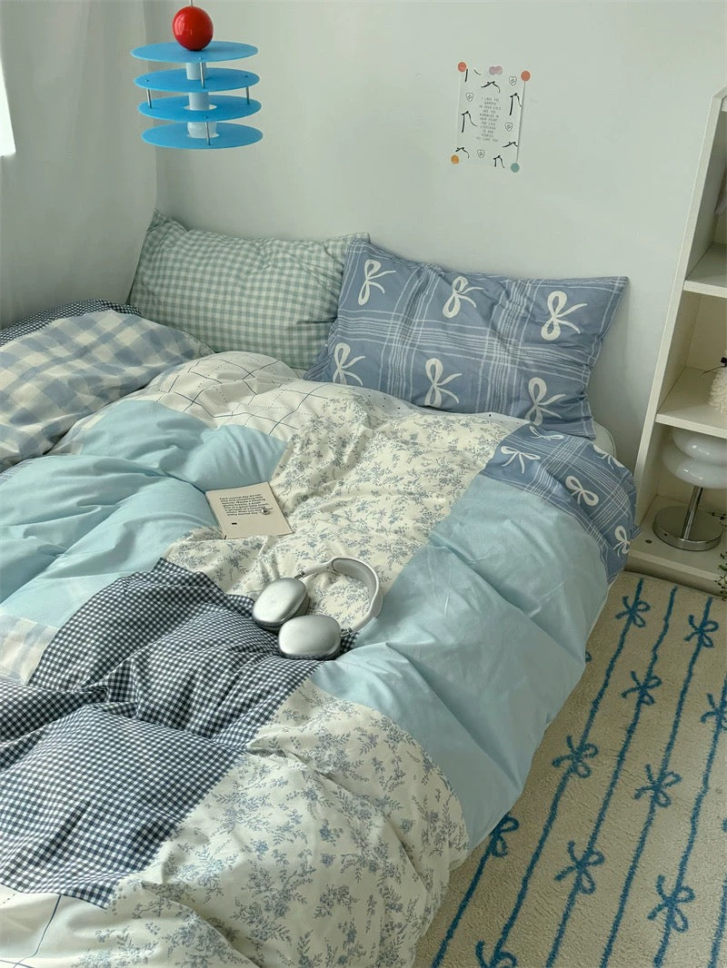 Bed with blue and white checkered and patterned bedding, pillows, and a small table with decor items.