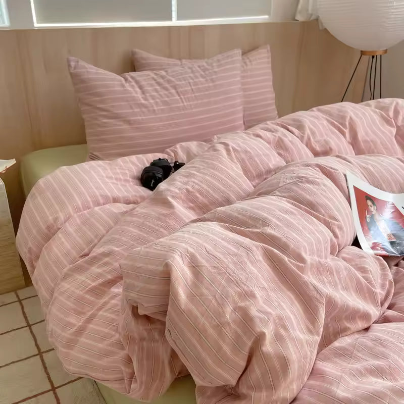 Pink striped bedding on a bed with pillows and a magazine.
