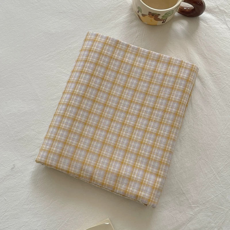 Plaid notebook on a textured surface with a cup in the background