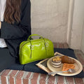 Green handbag next to a plate of food on a brick floor.