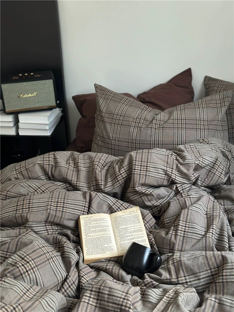Plaid blanket on a bed with an open book and a mug, next to a speaker.