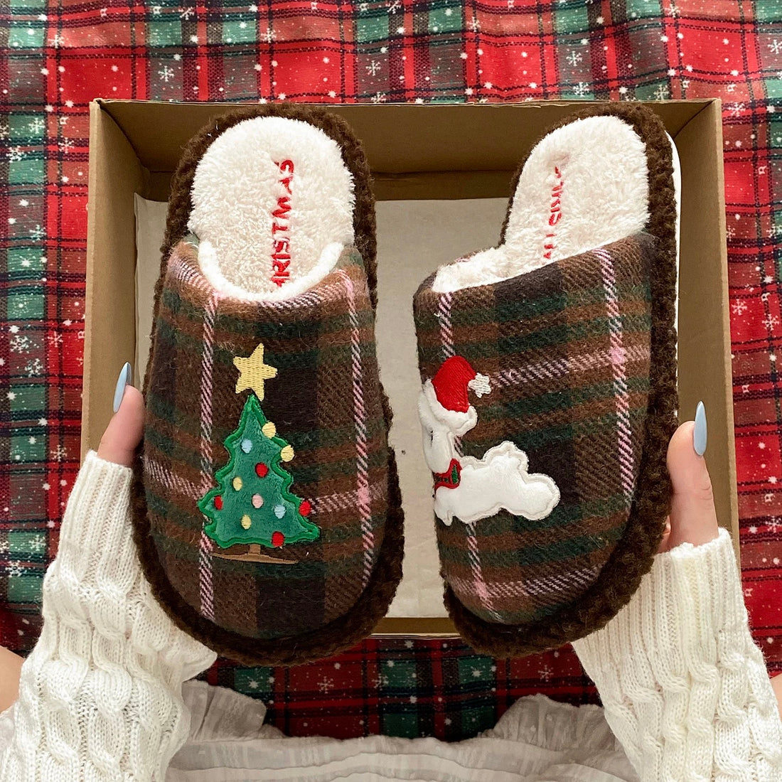 Blue plaid Christmas tree slippers with puppy motif held against a red tartan background