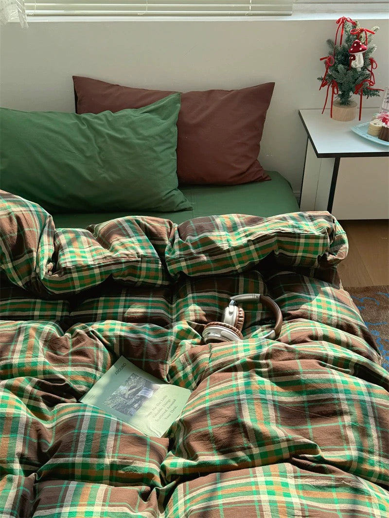 Plaid blanket on a bed with pillows and a small Christmas tree in the corner.