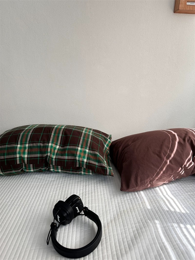 A plaid pillowcase lies beside a cocoa brown pillowcase.
