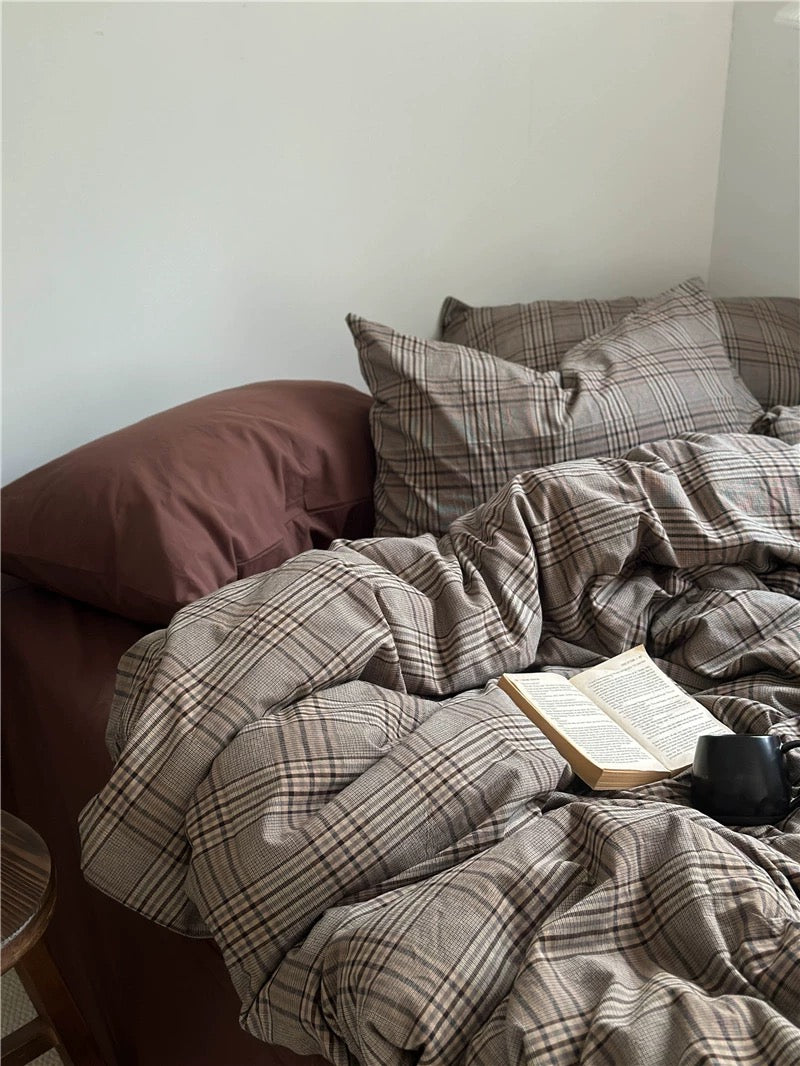 Plaid blanket draped over a sofa with pillows and a book on a light-colored wall background