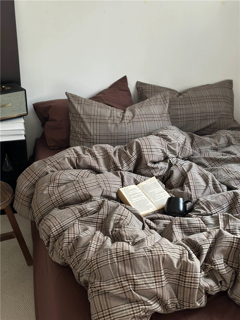 Bed with plaid comforter and pillows, featuring an open book and a mug.