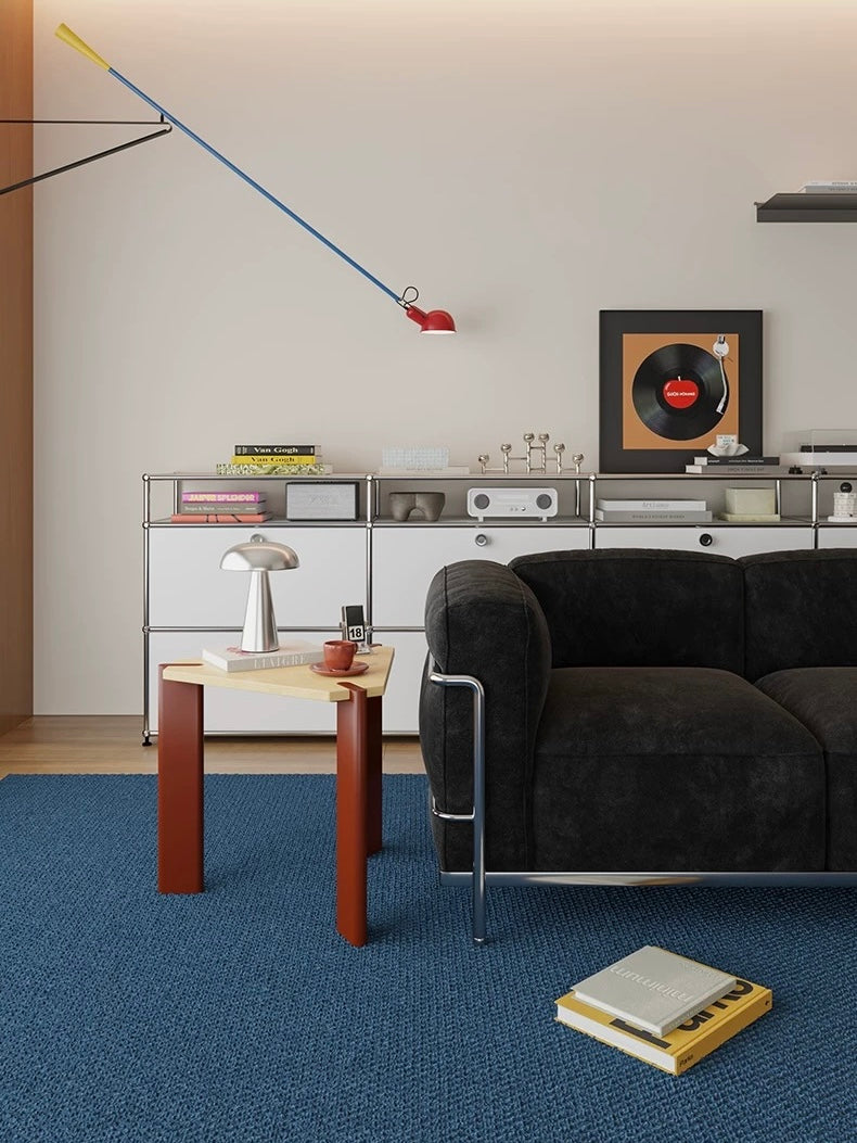 Burgundy side table with a triangular wood top seen beside a black sofa in a wide view of the room.