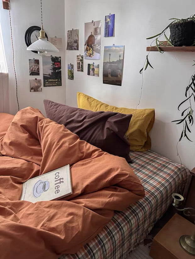 Bed with orange comforter and pillows, wall with pinned photos and a plant