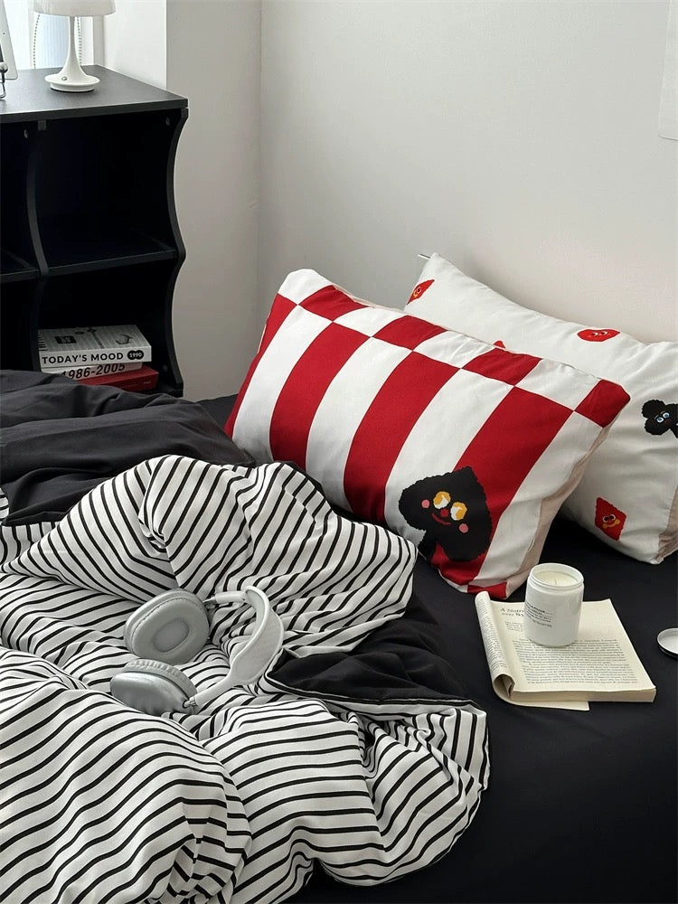 Red and white striped pillow with black cat design on a bed with black and white striped bedding.