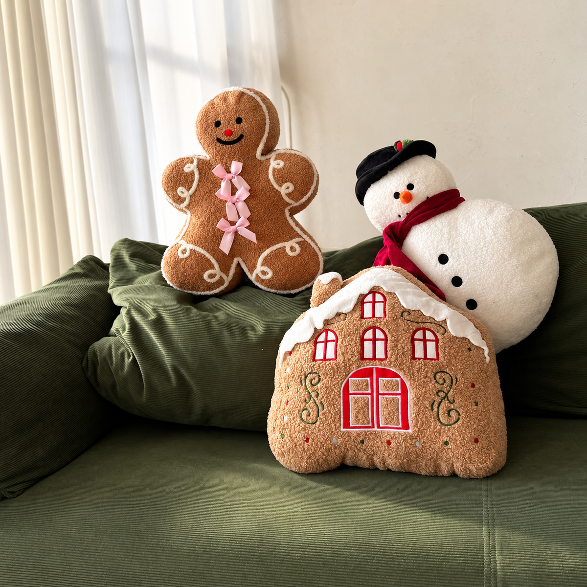 Gingerbread man, snowman and gingerbread house Christmas pillows arranged together on a green sofa
