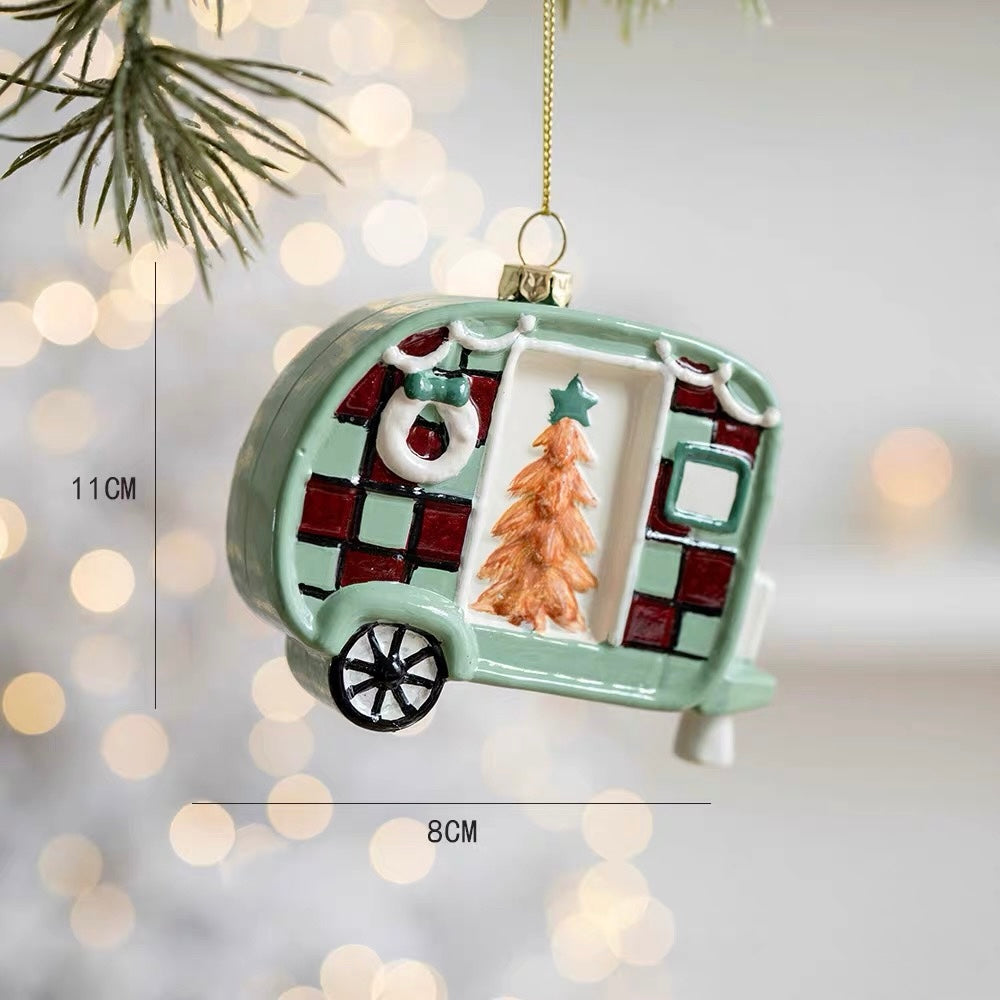 A Christmas tree camper ornament has checked red and green panels, a tree design and a black wheel.
