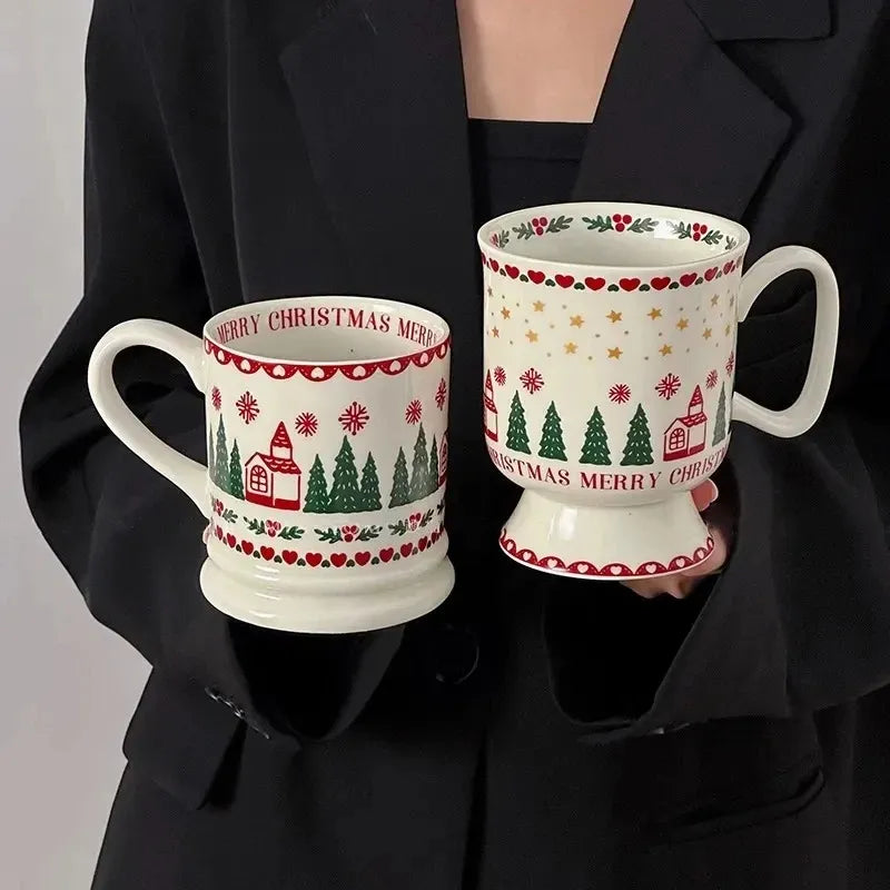Two ceramic Christmas mugs with festive red and green holiday patterns and gold stars, held by a person wearing a black blazer.