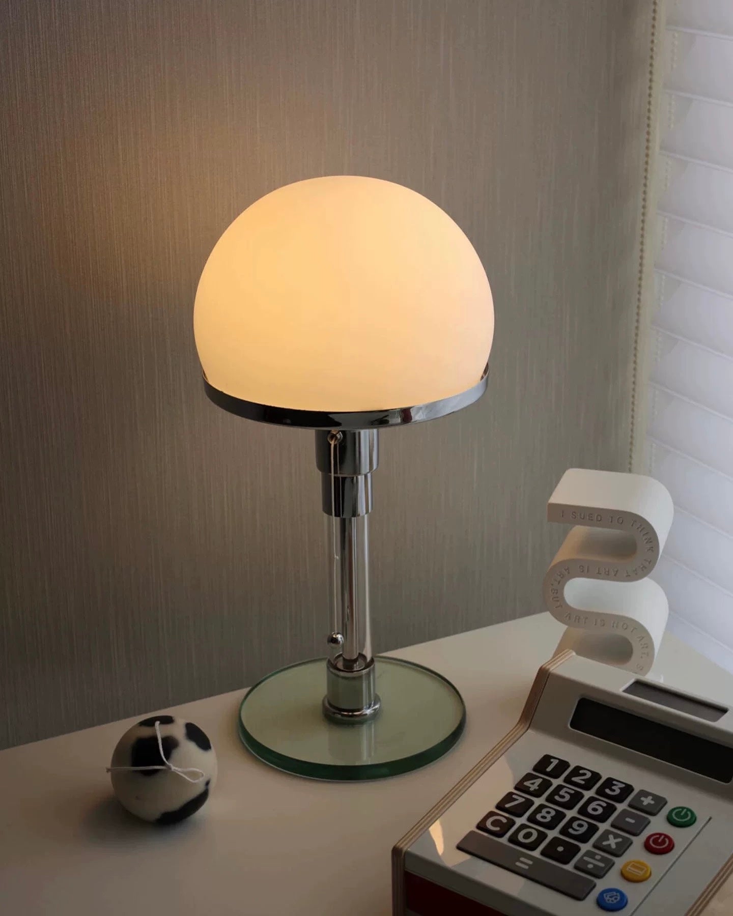 Chrome mushroom table lamp with warm dome shade styled on white bedside table with books.