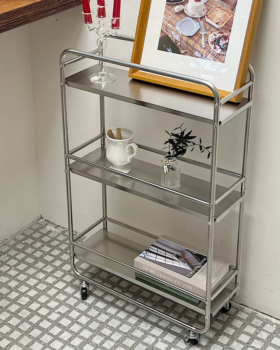 Chrome rolling bar cart styled with candles, books, and framed art in minimalist room corner.