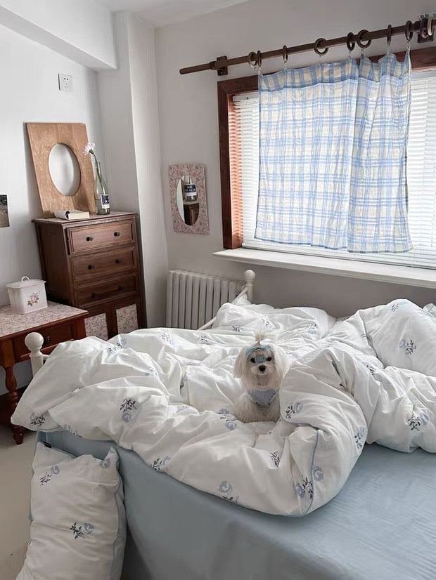 Bedroom with a bed covered in white bedding, wooden dresser, and window with plaid curtain.