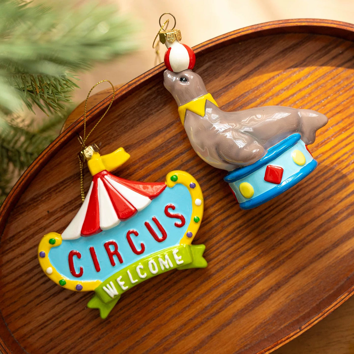 Colorful Christmas ornaments show a gray seal balancing a ball beside a circus sign with a striped roof.