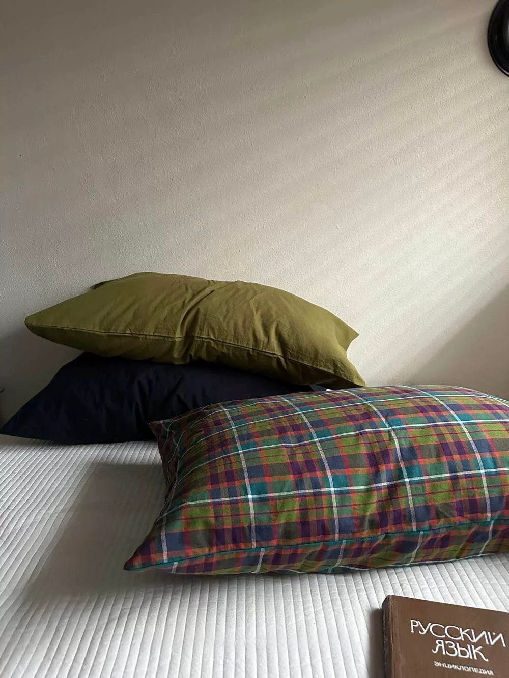 Multicolor plaid pillowcases layered over olive green and navy on a white bed.