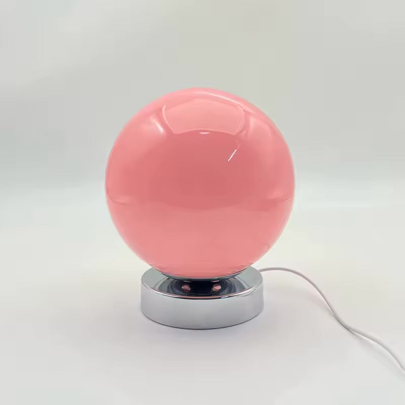 Pink spherical lamp with a metallic base on a white background