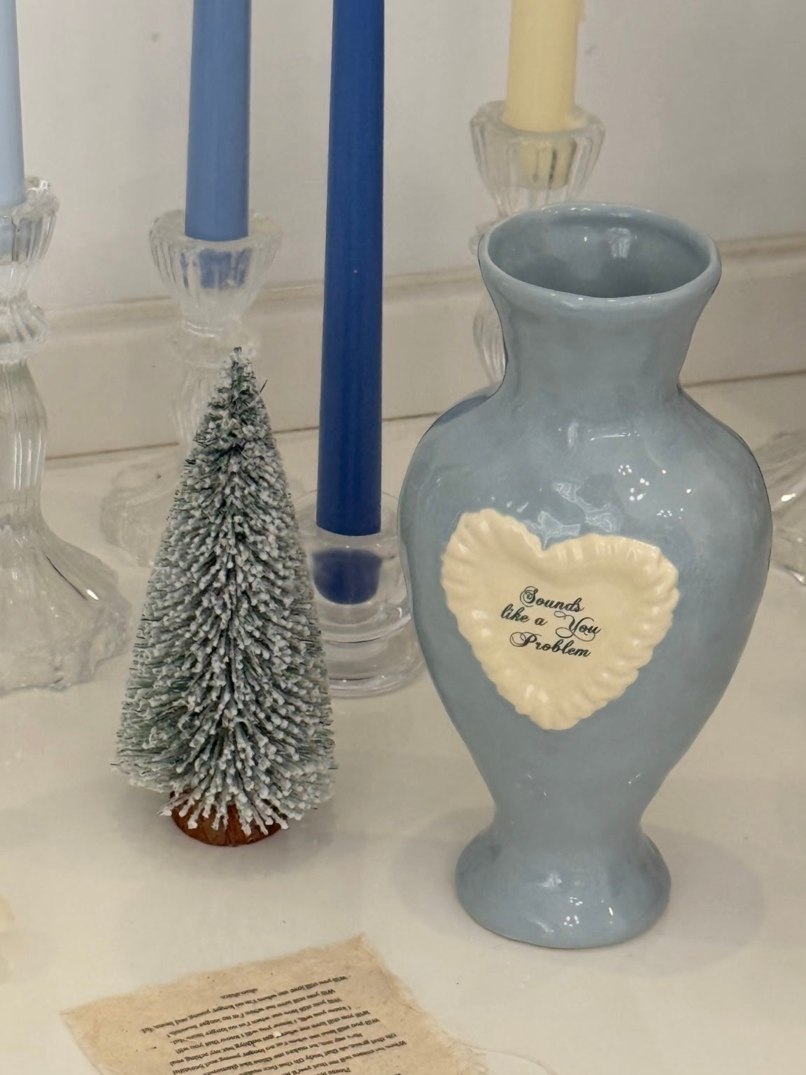 Coquette decor vase beside taper candles and a small Christmas tree, showing its blue glaze and white heart.