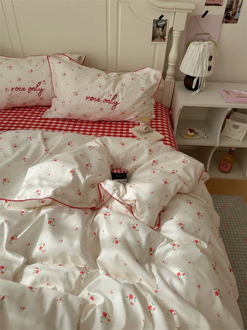 Bedding set with floral pattern and 'rose only' text on a bed with red checkered blanket.
