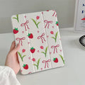 White tablet case with strawberry, tulip, and bow pattern held by a hand on a light gray background.